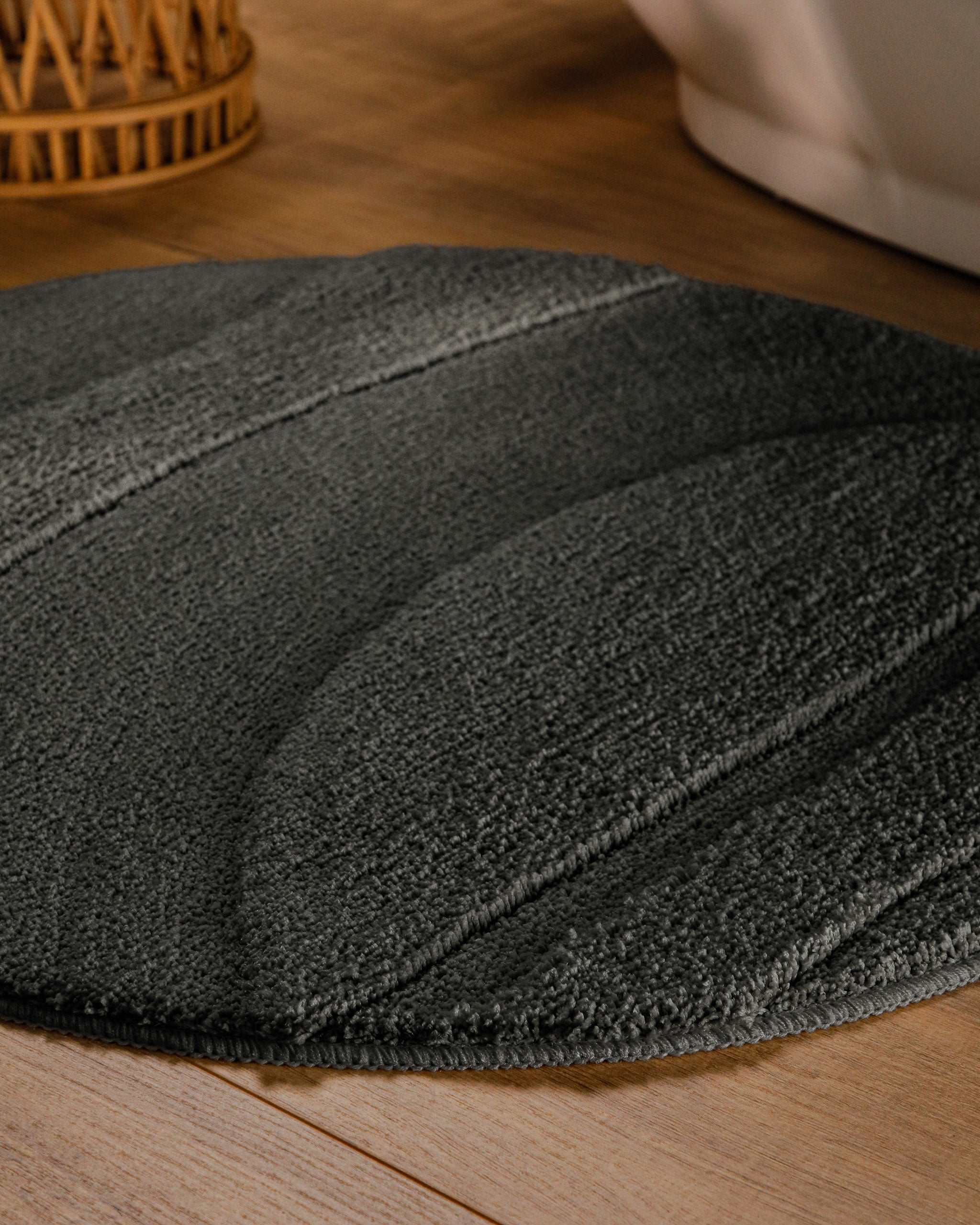 Badteppich von BathKing by WECONhome Marc Anthrazit Grau rund im Badezimmer auf Holzboden neben Badewanne, Florstruktur und Linienrelief erkennbar