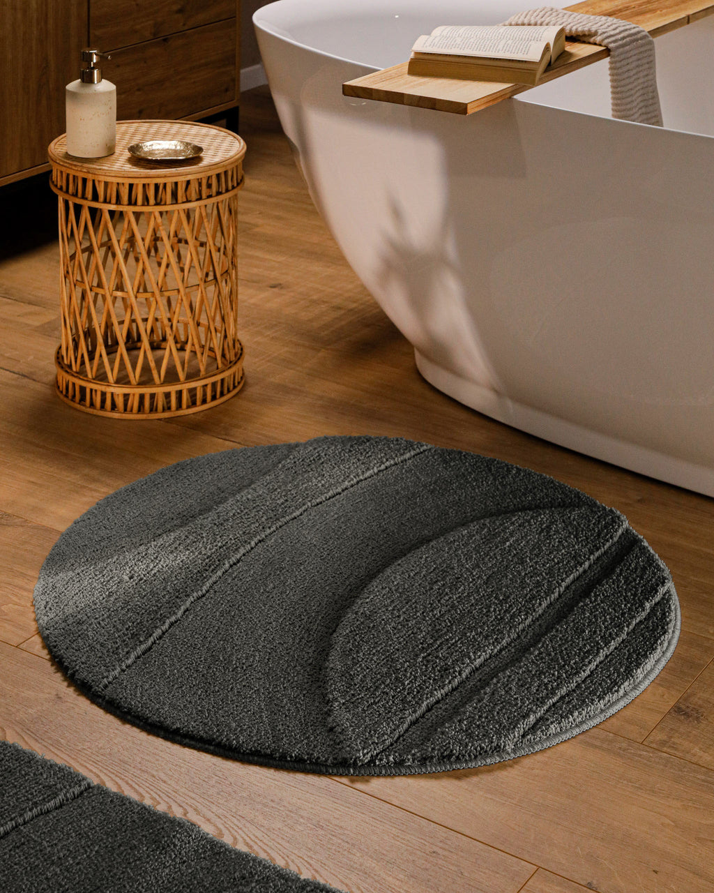 Runder Badteppich von BathKing by WECONhome Marc Anthrazit Grau im Badezimmer vor Badewanne auf Holzboden, strukturiertes Linienrelief im Flor sichtbar
