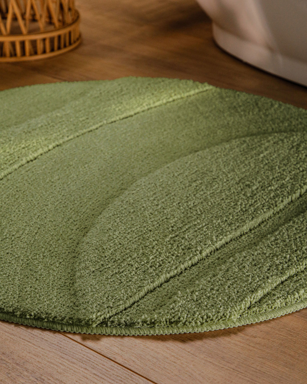 Badteppich von BathKing by WECONhome Marc Reseda Grün rund im Badezimmer auf Holzboden neben Badewanne, Florstruktur und Linienrelief erkennbar