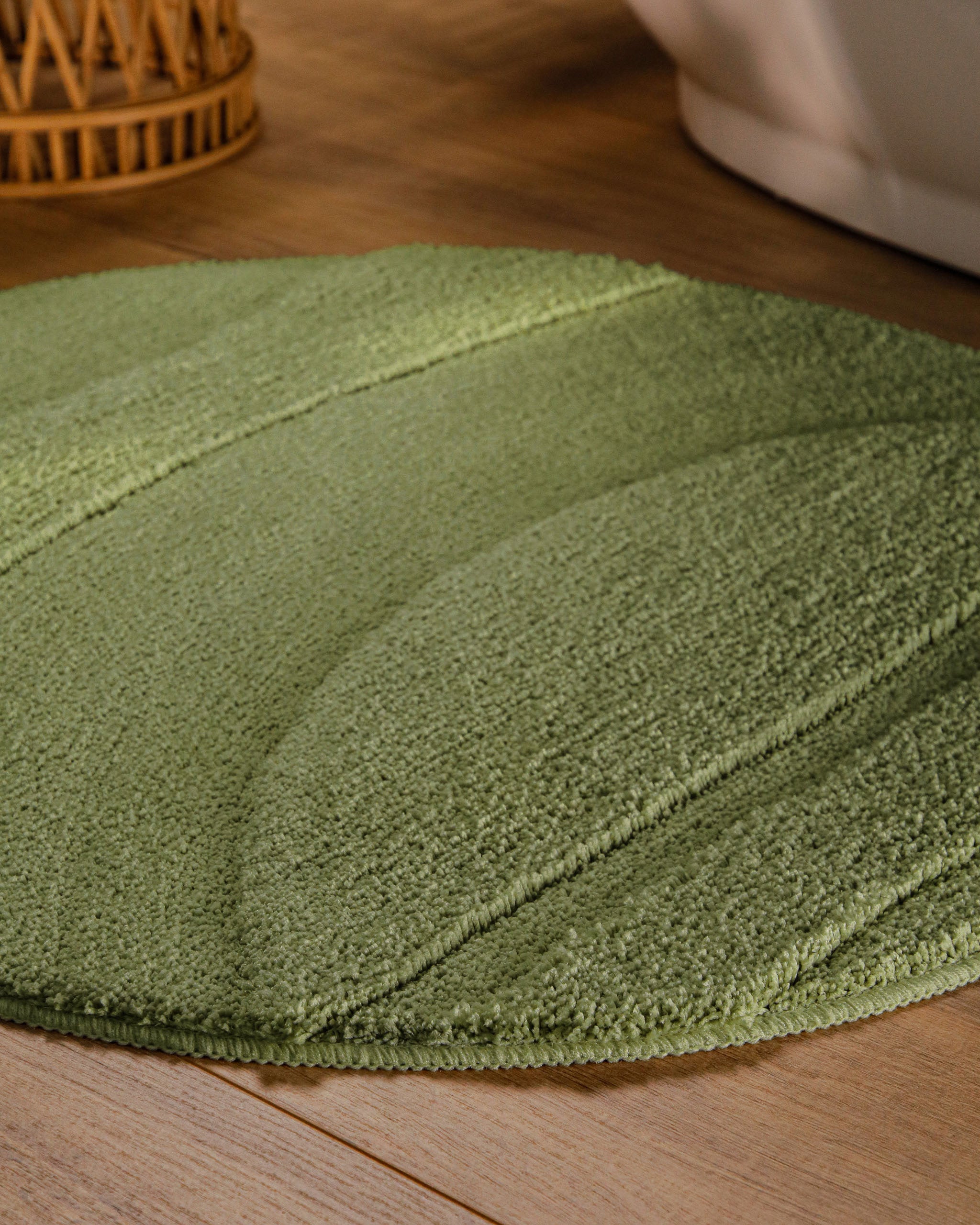 Badteppich von BathKing by WECONhome Marc Reseda Grün rund im Badezimmer auf Holzboden neben Badewanne, Florstruktur und Linienrelief erkennbar