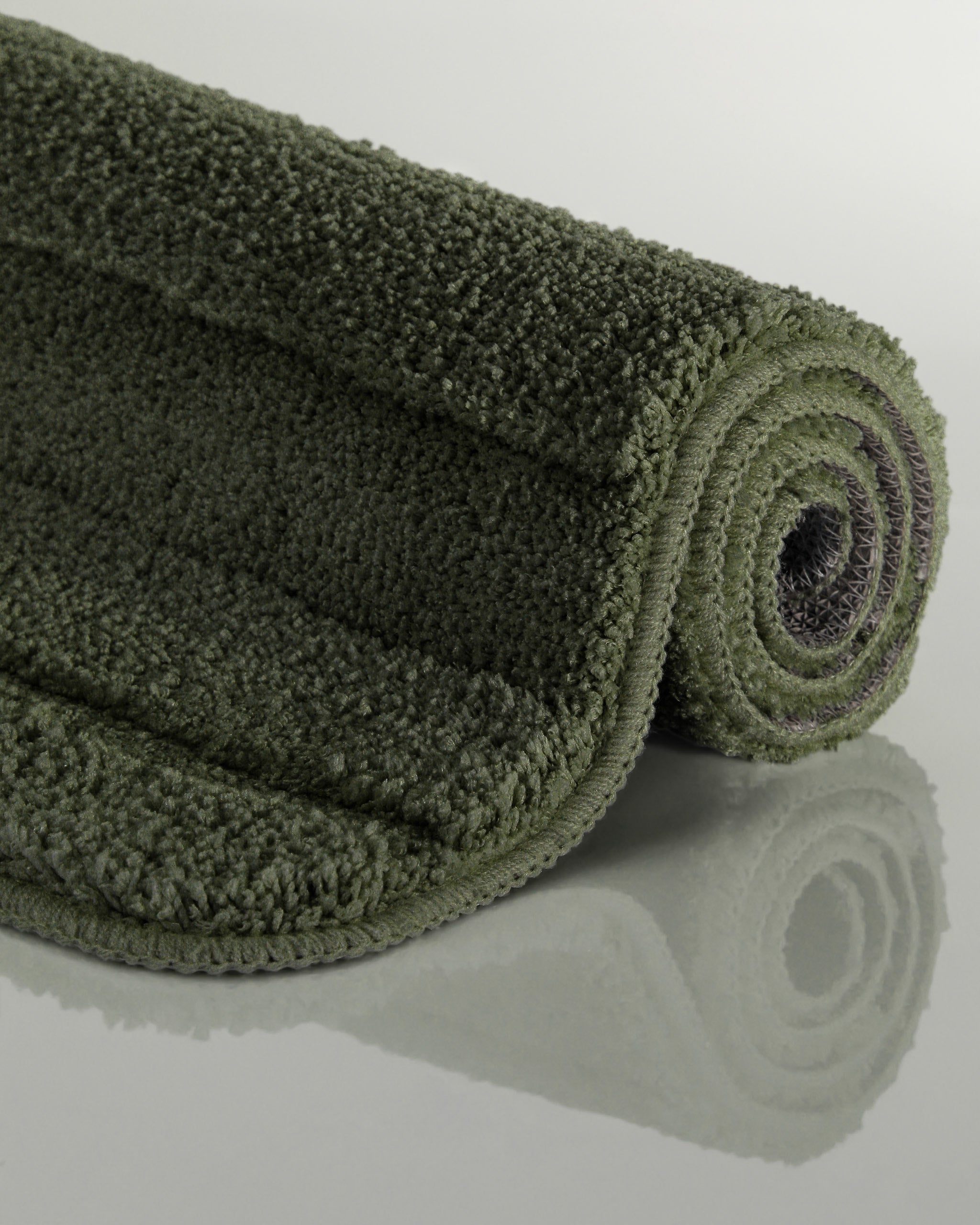 Badteppich von BathKing by WECONhome Marc Kiefer Grün aufgerollt auf hellem Hintergrund, Seitenansicht zeigt Florhöhe und Teppichkante