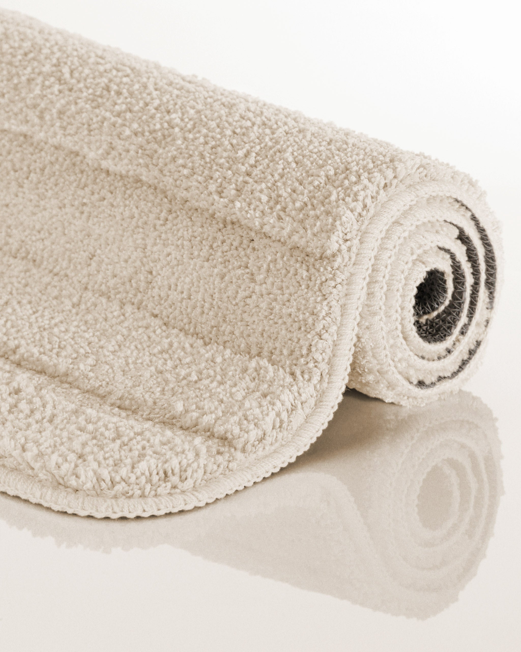 Badteppich von BathKing by WECONhome Marc Creme Weiß aufgerollt auf hellem Hintergrund, Seitenansicht zeigt Florhöhe und Teppichkante
