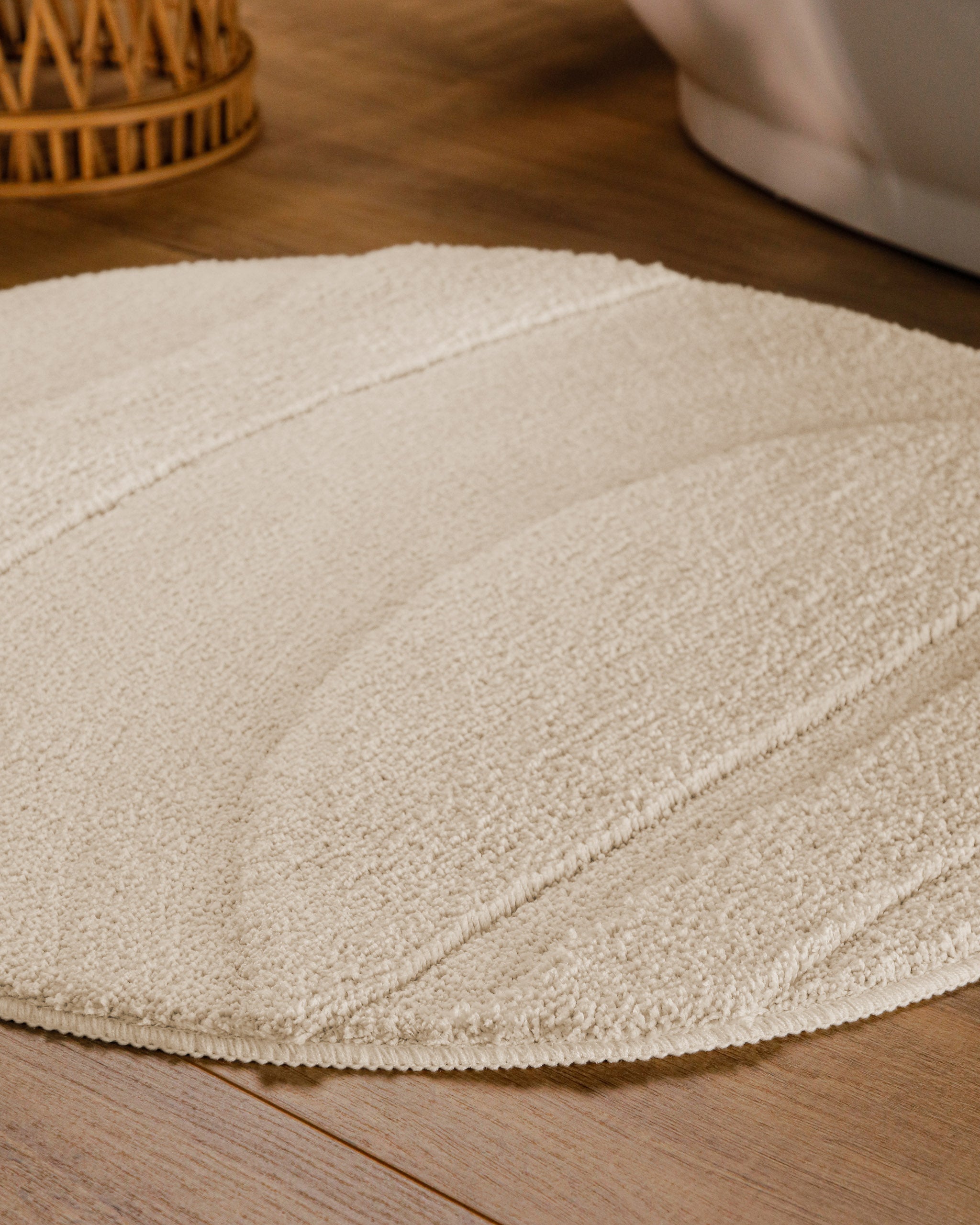 Badteppich von BathKing by WECONhome Marc Creme Weiß rund im Badezimmer auf Holzboden neben Badewanne, Florstruktur und Linienrelief erkennbar