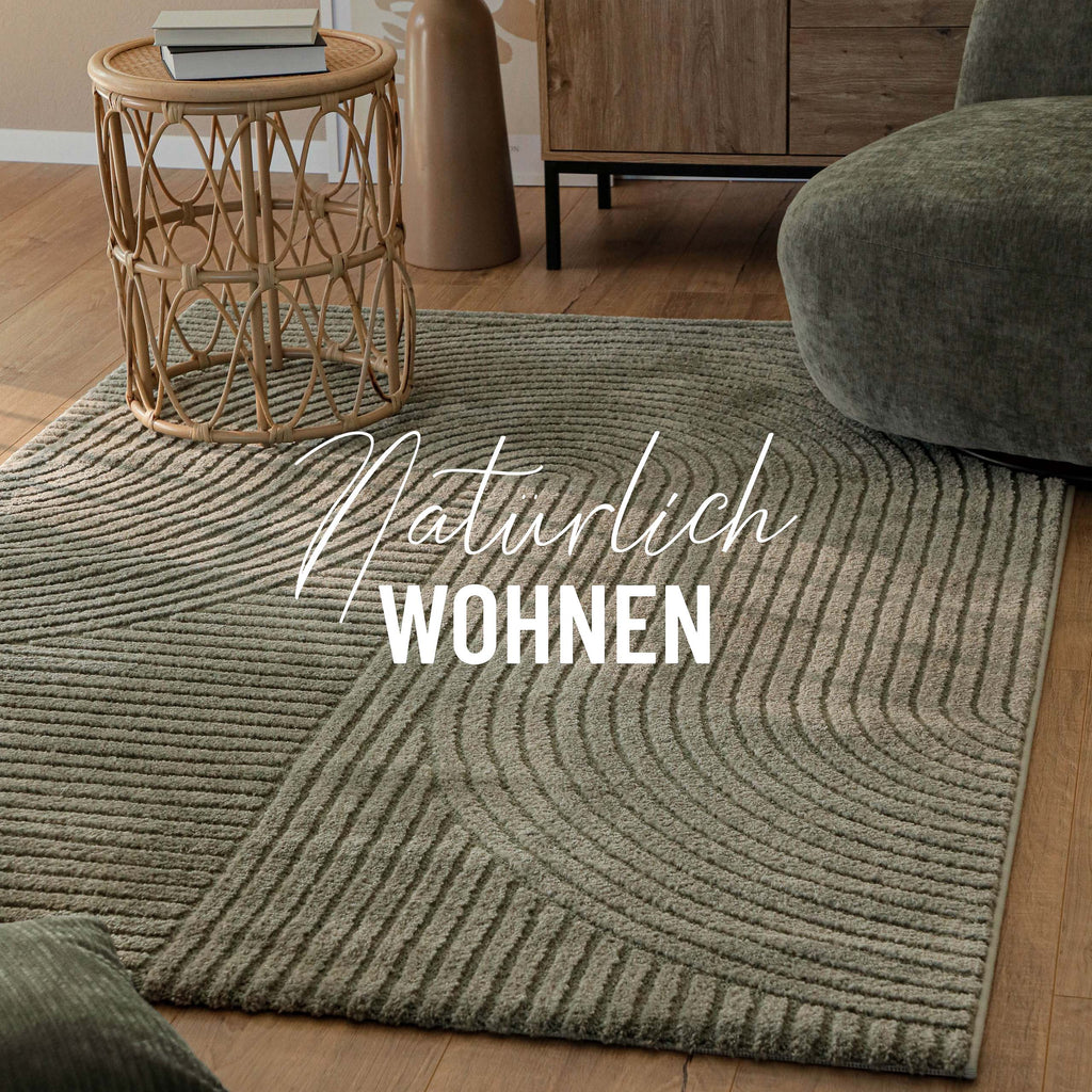 Grafik: Teppich Bolen oliv grün im Wohnzimmer neben Korbtisch und Sofa, Holzboden, Natürlich Wohnen