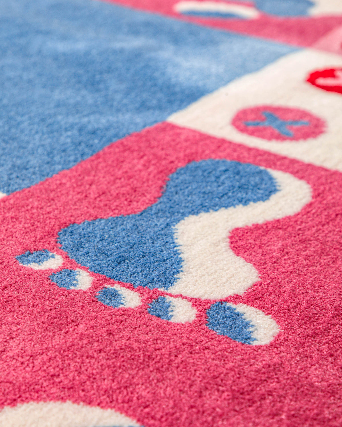 Detailaufnahme des Kinderteppichs Hand&Feet mit blauem und weißem Fußabdruck-Motiv auf rosa Untergrund