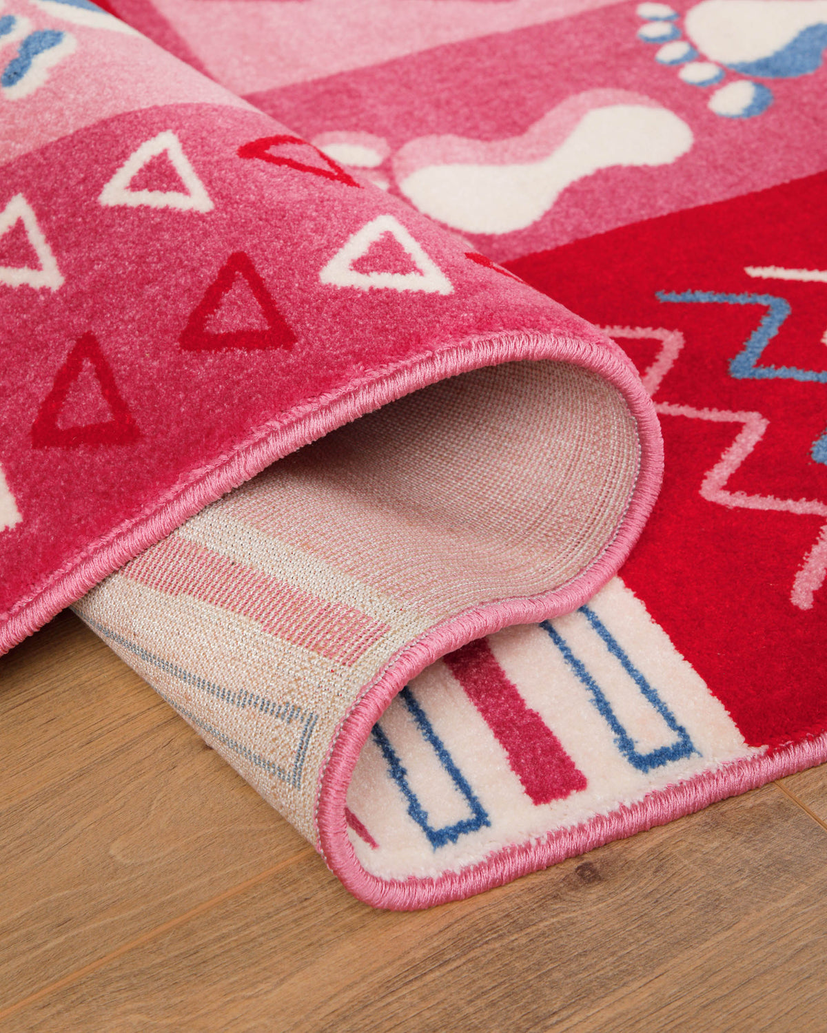Kinderteppich Hand&Feet, umgeschlagene Ecke zeigt Teppichrücken und pinke Bordüre mit weißem Zickzack-Muster