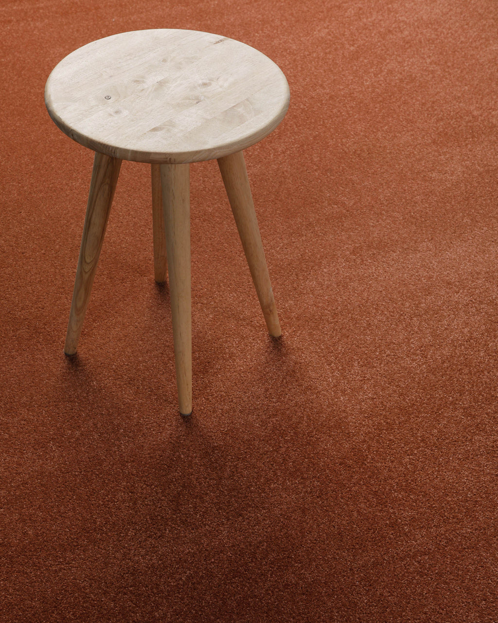 Kurzflor Teppich Montepulciano Ziegel Rot im Wohnraum mit Hocker auf warmer Oberfläche