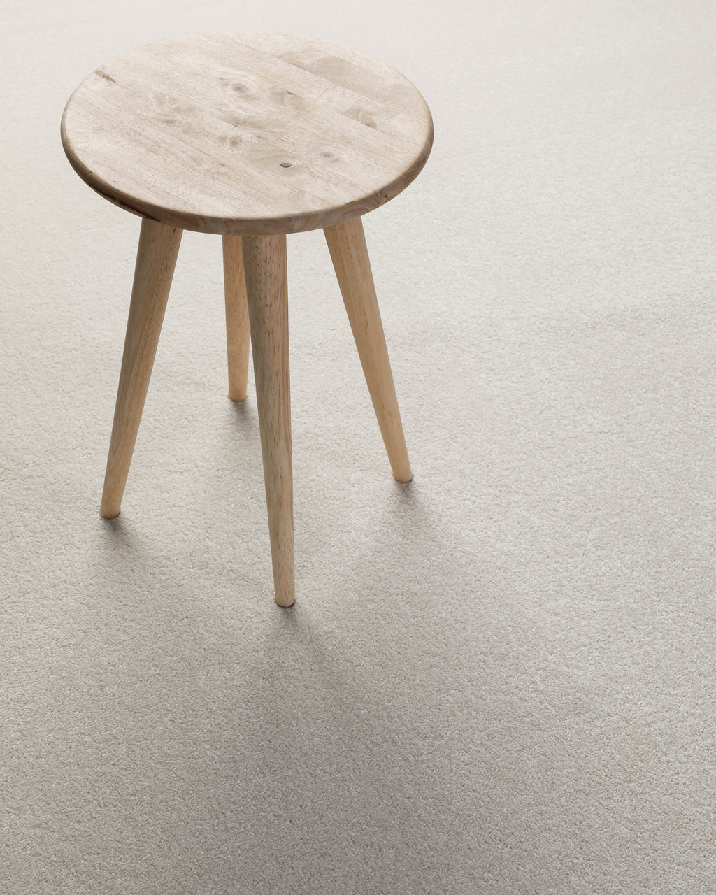 Kurzflor Teppich Montepulciano Creme Weiß im Wohnraum mit Hocker auf heller, ruhiger Oberfläche