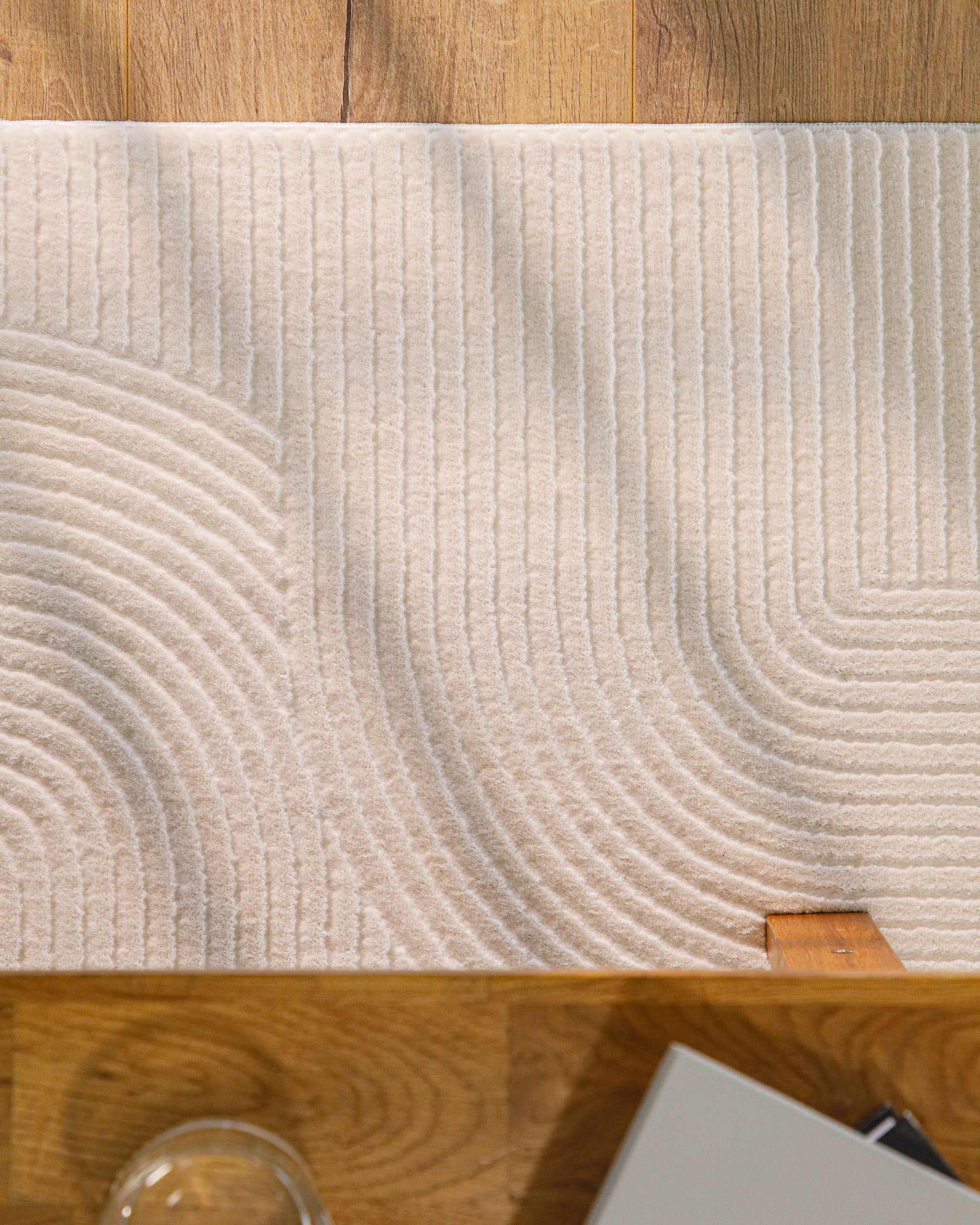 Detailansicht WECONhome Kurzflorteppich Nuuk Arc in Creme Weiß unter einem Holztisch