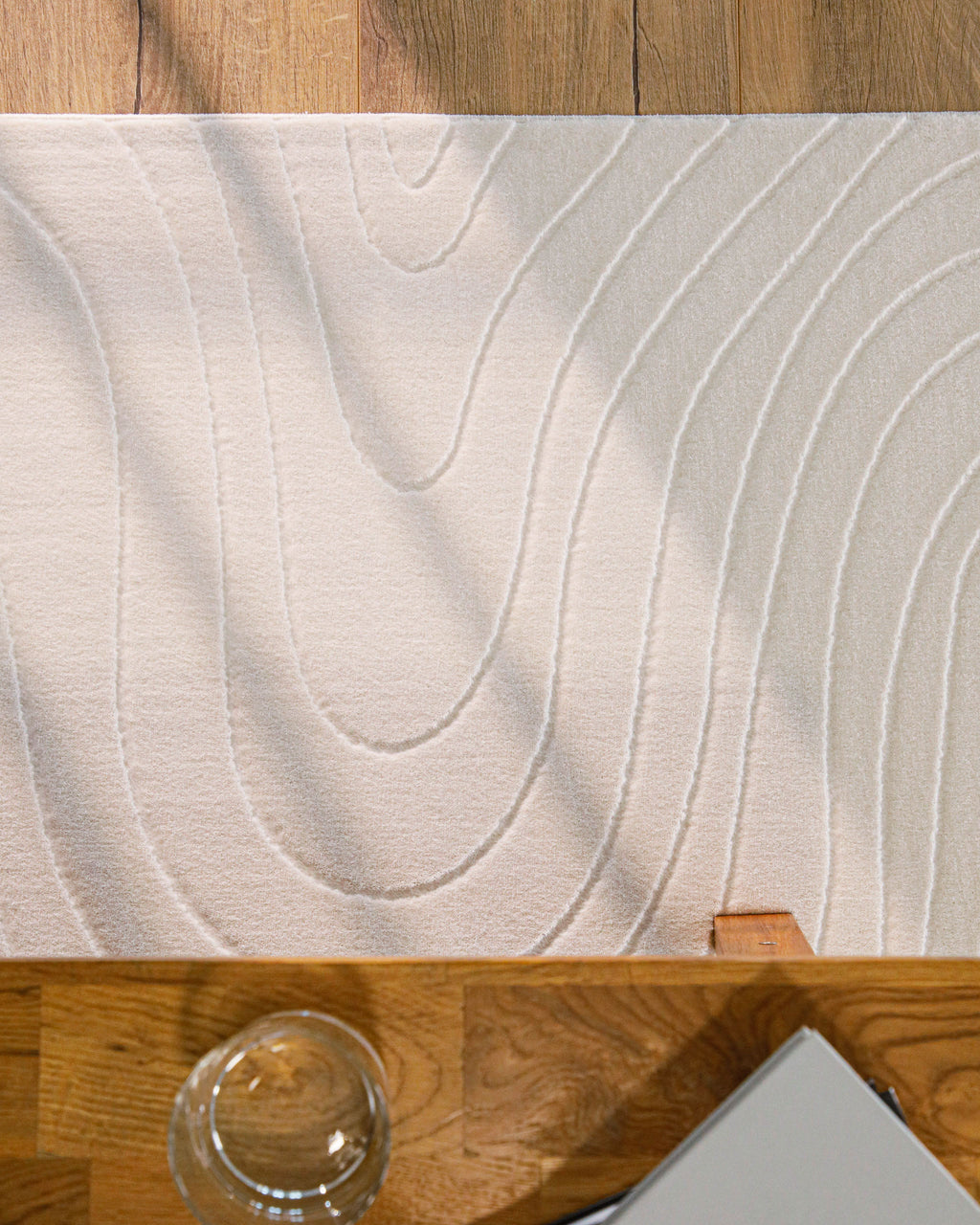 Kurzflor Teppich creme-weiß Hoch-Tief-Wellenstruktur Detailansicht unter einem Holztisch