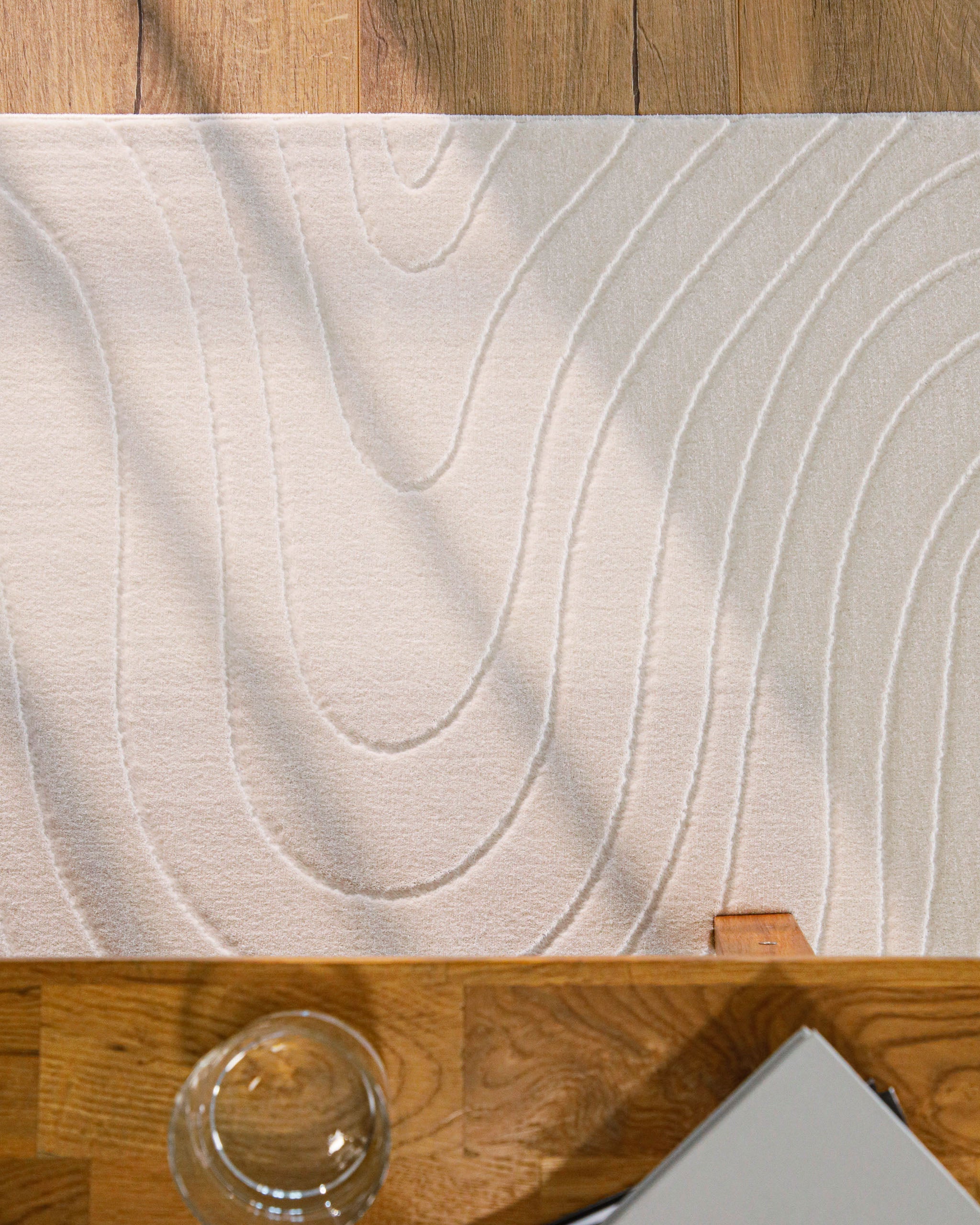 Kurzflor Teppich creme-weiß Hoch-Tief-Wellenstruktur Detailansicht unter einem Holztisch