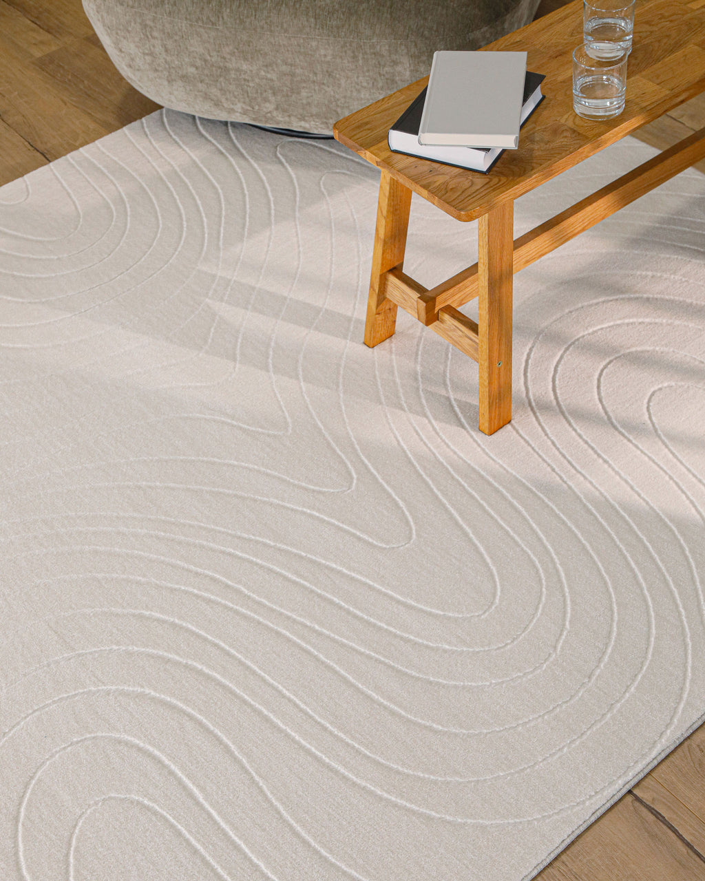 Nuuk Flow Teppich creme-weiß in hellem Wohnzimmer unter einem Holztisch und Hocker