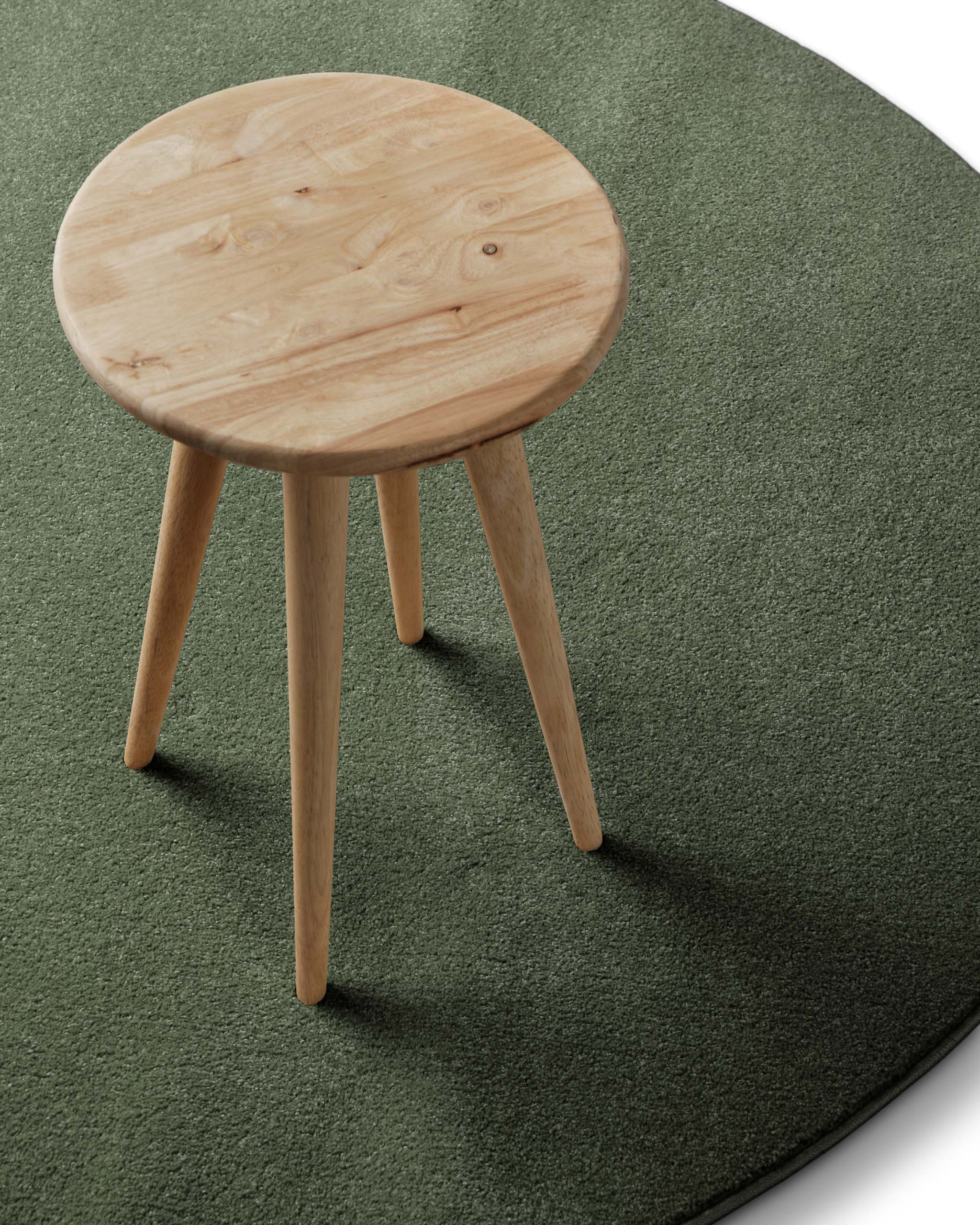 Kurzflor Teppich Freja Laub Grün rund im Wohnraum mit Hocker, zeigt natürliche Farbwirkung im Raum